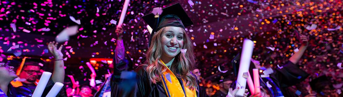 A graduate smiles and waves at PCC graduation ceremony